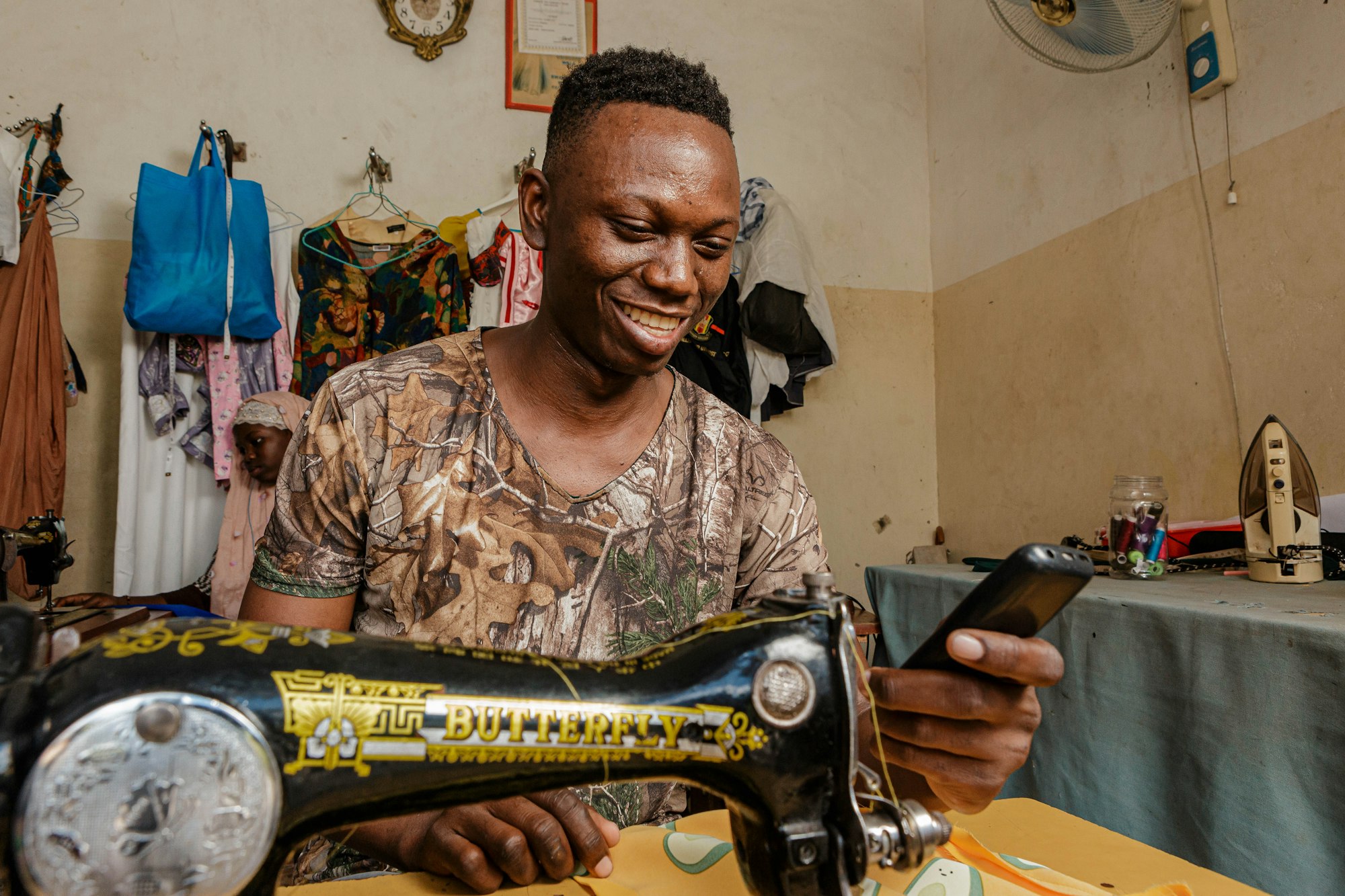 A smiling tailor at his sewing machine, reading his phone